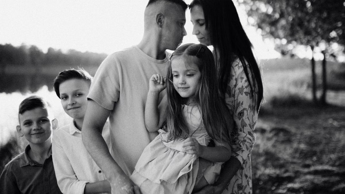 A serene black and white portrait of a family standing by a lake.